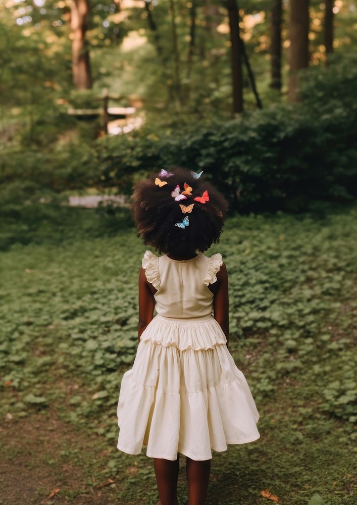 A black girl wearing cream dress and a colorful butterflies hair clip in the green yard kid celebration hairstyle. AI…