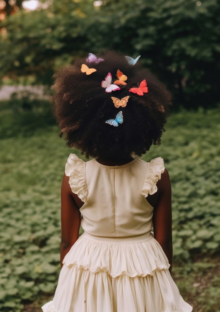 A black girl wearing cream dress and a colorful butterflies hair clip in the green yard kid hairstyle butterfly. AI…
