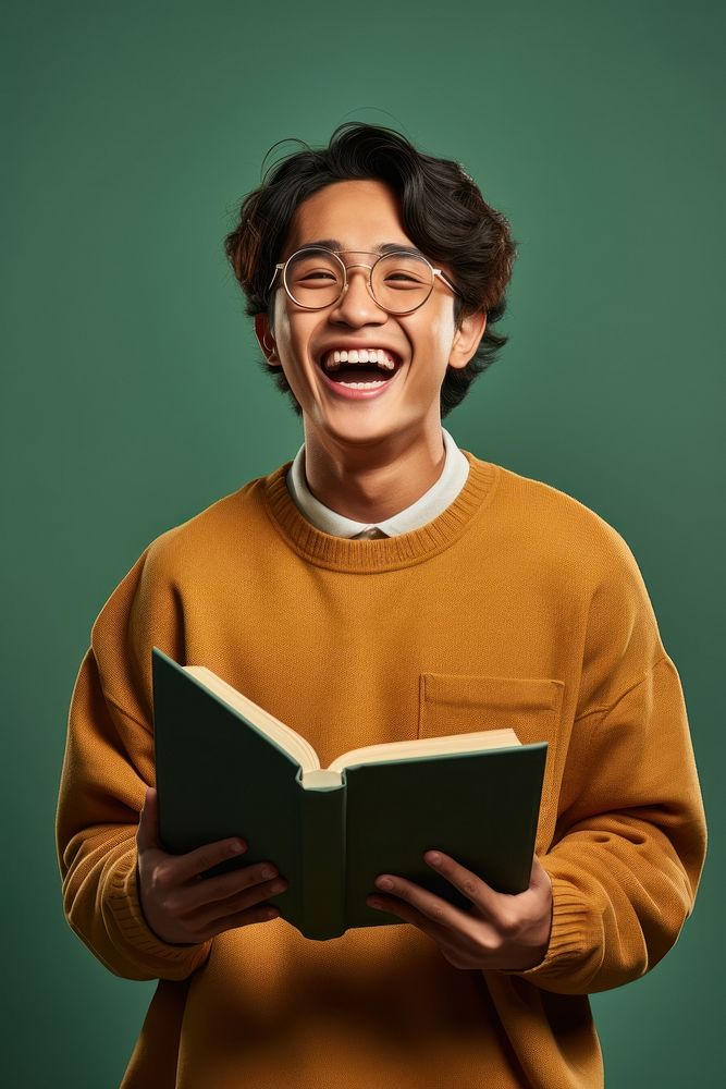 Mixed asian student holding a book glasses publication laughing. AI generated Image by rawpixel.