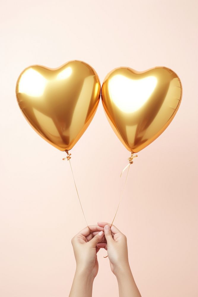 Two hands hold an aluminium gold hearts shaped balloon celebration anniversary chandelier. AI generated Image by rawpixel.