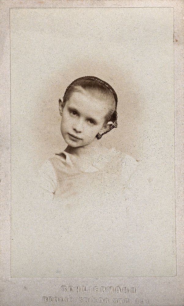 A girl wearing a hairnet, head tilted to one side: a vignetted head-and-shoulders portrait. Photograph by O. Schliepmann…