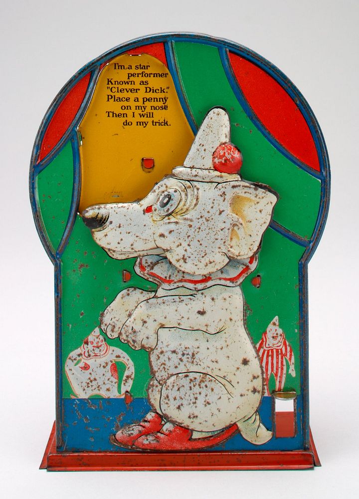 front relief panel of white dog wearing hat, ruffled collar and shoes, with 2 clowns in background; red box and platform on…