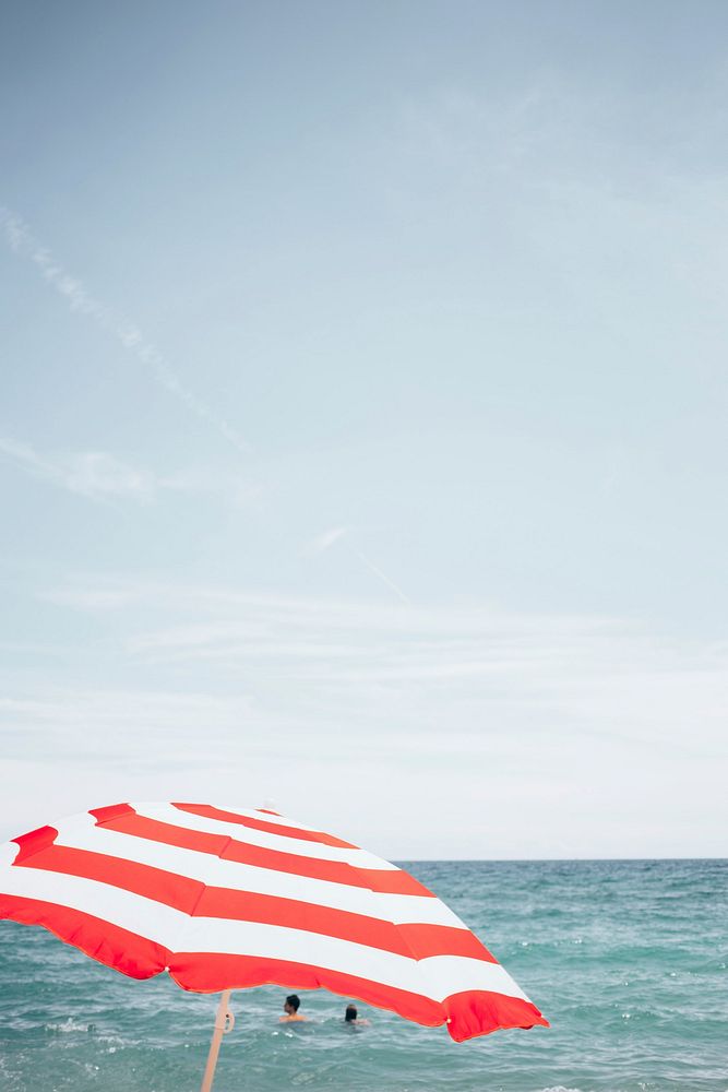 Red & white striped beach umbrella, ocean background. Free public domain travel CC0 photo.