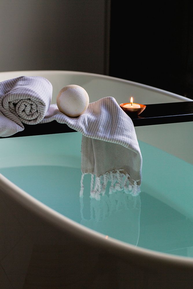 Bath bomb on wooden tray over spa tub with lit candle and towel, free public domain CC0 image.