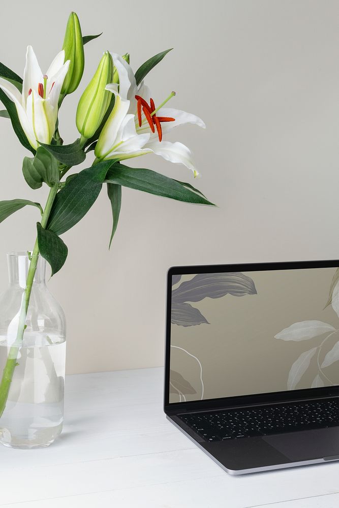Laptop with aesthetic desktop wallpaper, lily in vase aside