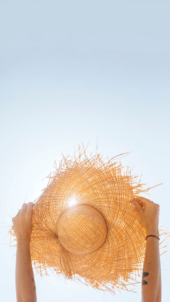 Tattooed arm raising a straw hat up in the sky mobile phone wallpaper