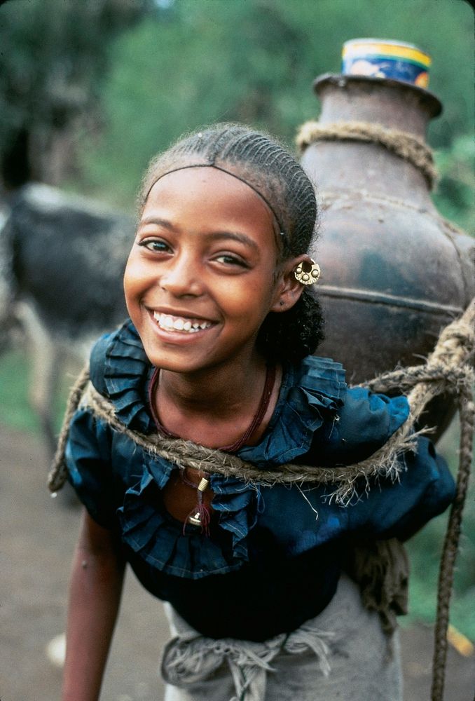 Beautiful smiling girl, as she carries a heavy load of water home. Original public domain image from Flickr