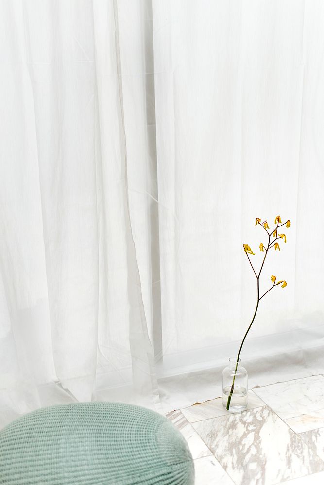 Yellow forsythia in a cleared-vase on a white marble floor by a white curtain