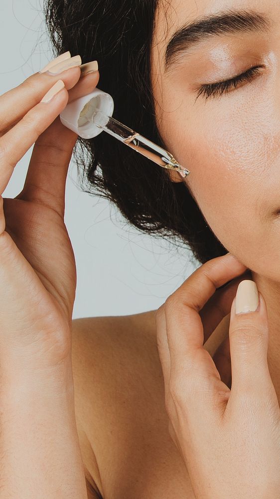 Young woman applying serum on her face 