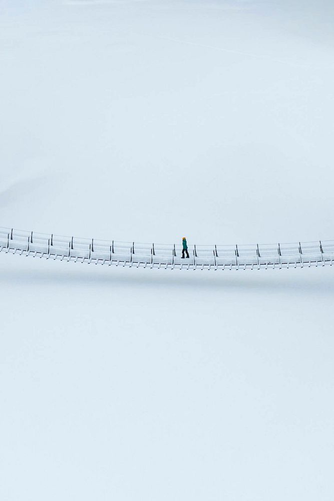 Woman crossing a suspension bridge in a snowy Oulanka National Park, Finland drone shot