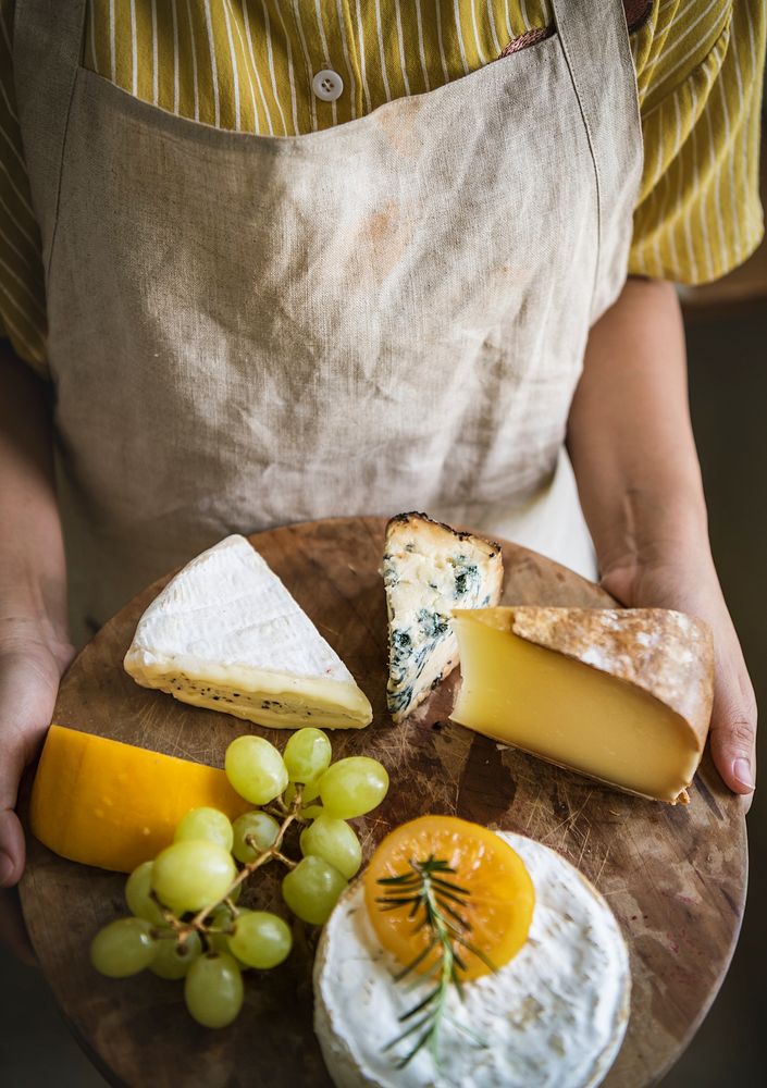 Person holding a platter of green grapes and different types of cheese