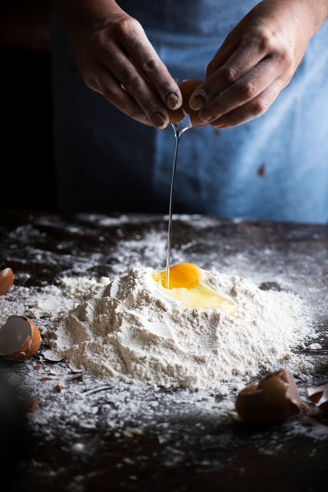 Baker cracking egg into flour