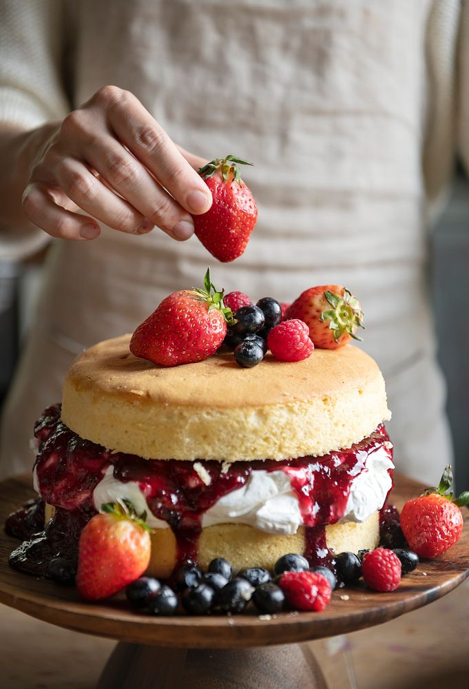 Woman decorating a layered cake with berries