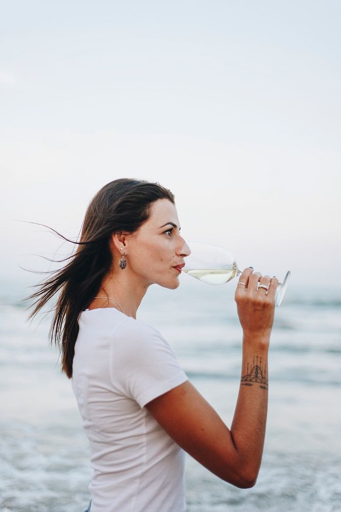 Woman drinking a glass of wine by the beach