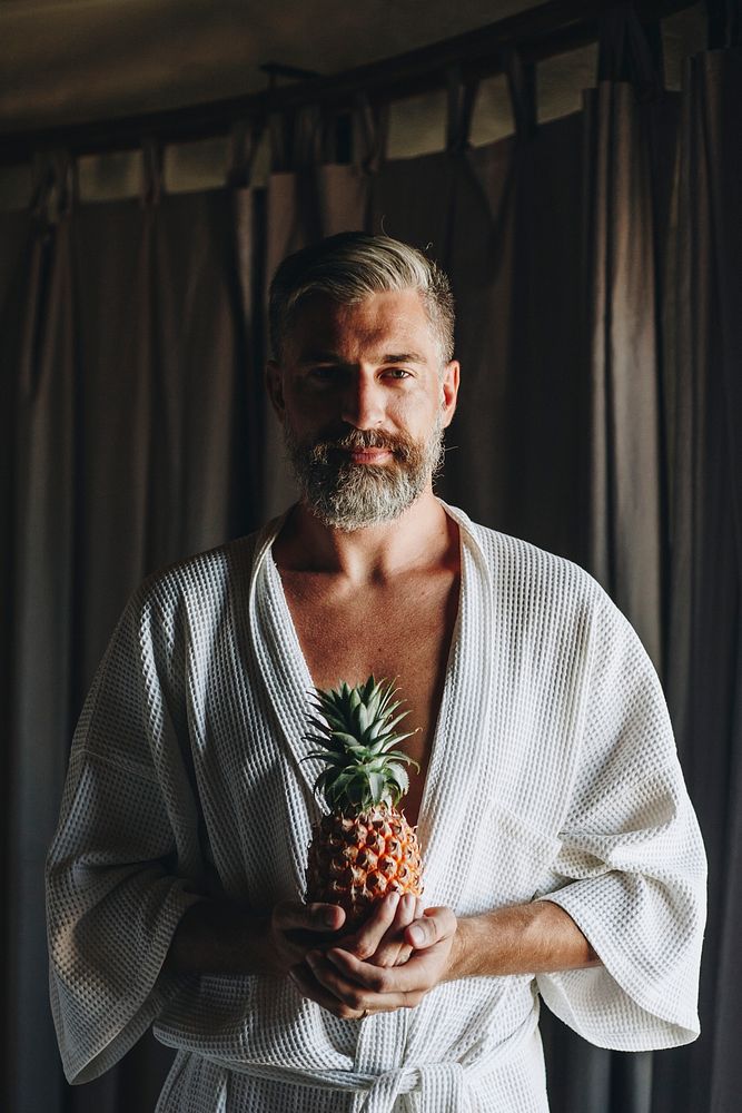 Man in a bathrobe holding a pineapple
