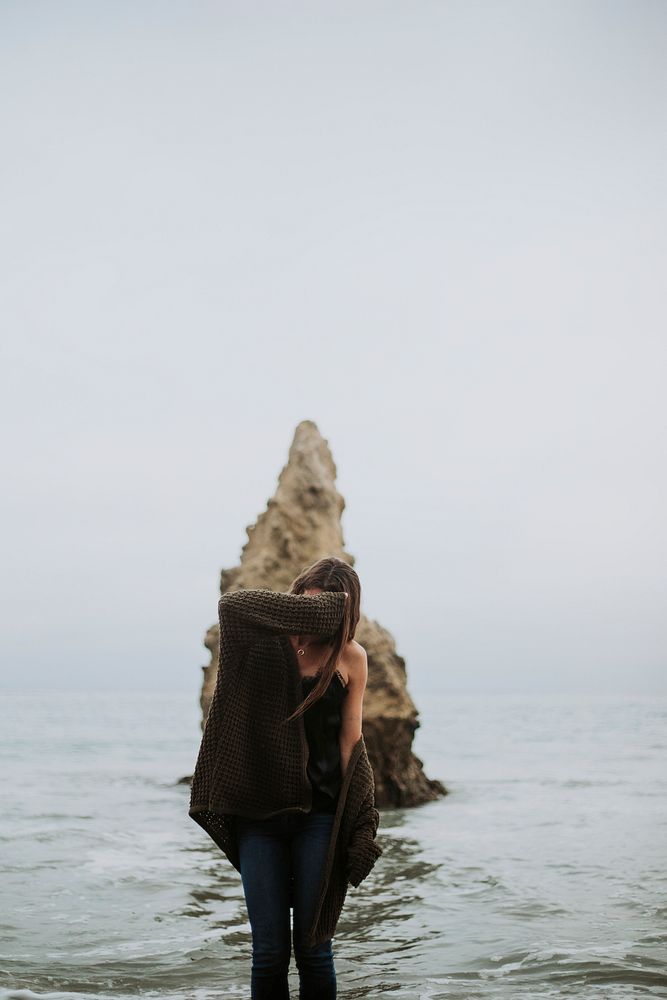 Woman standing at the beach covering her face