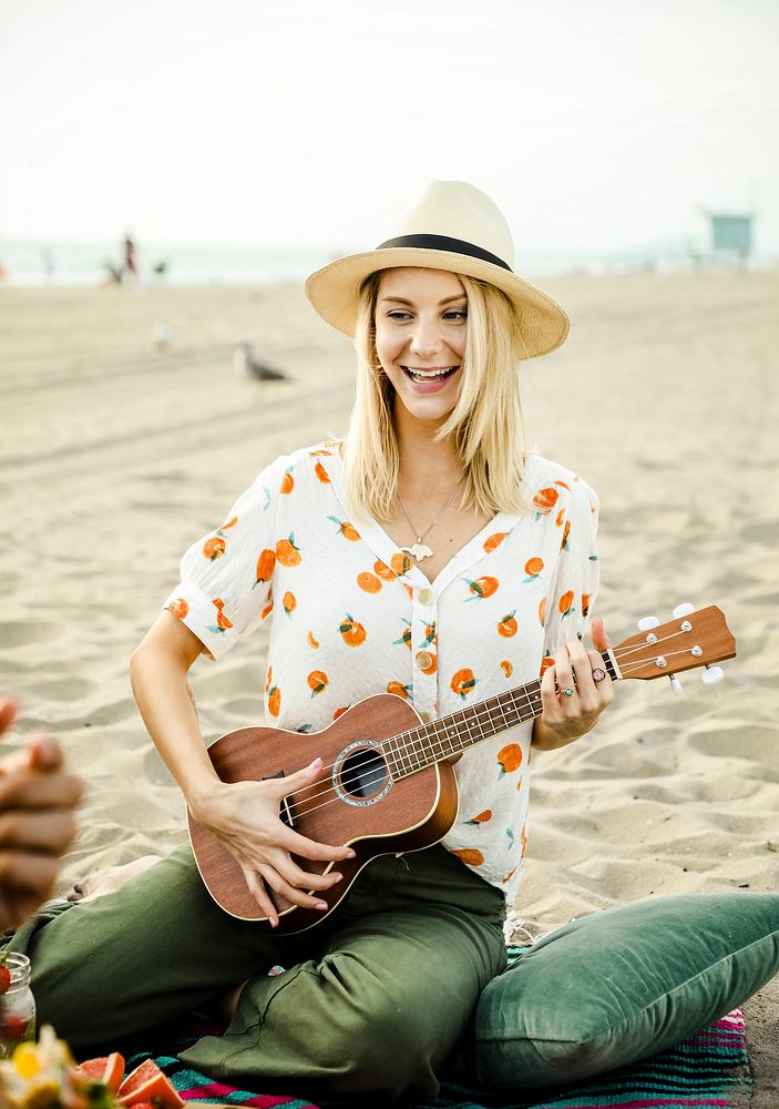 Blond girl playing ukulele for her friends at the beach