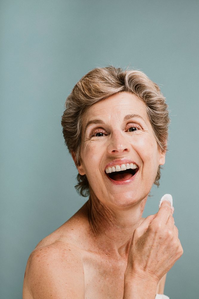 Cheerful elderly woman wiping her face with a cotton pad