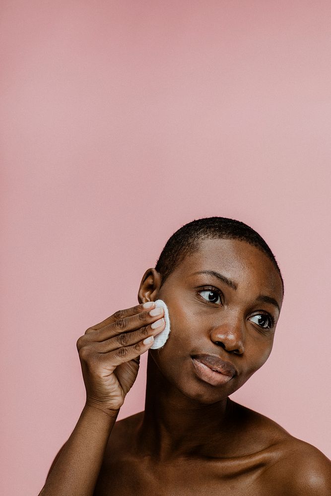 Black woman wiping her face with a cotton pad