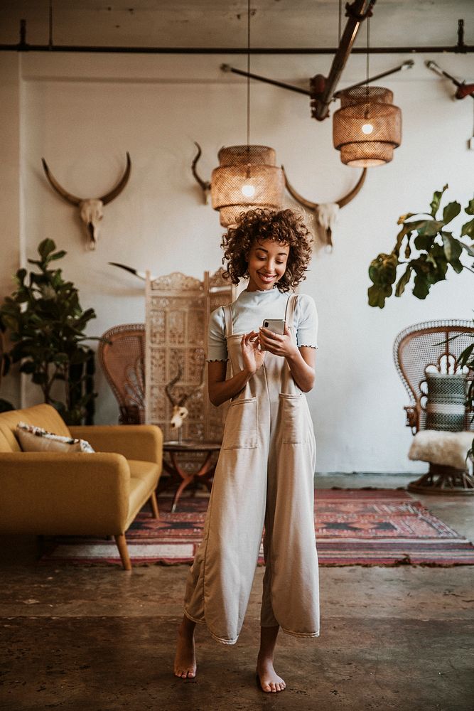 Cheerful black woman using her phone in living room