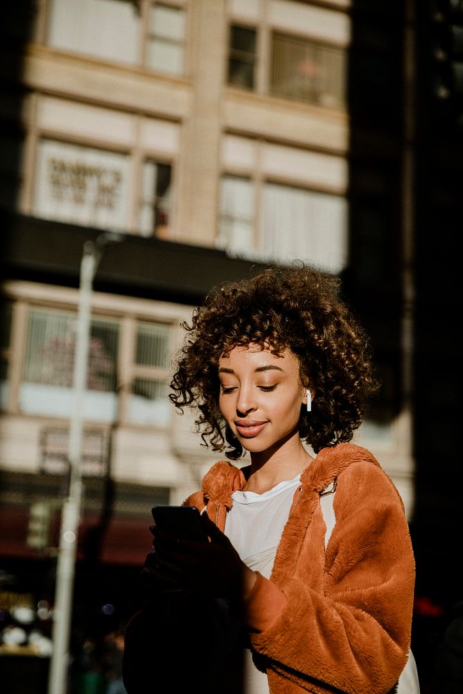 Cheerful black woman listening to music while walking in downtown