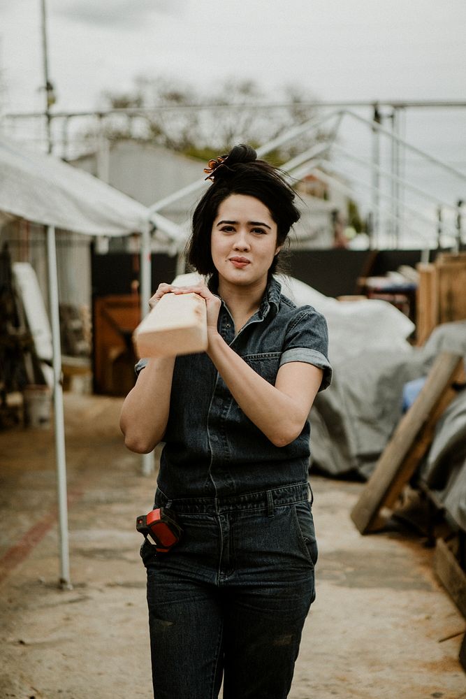 Female carpenter carrying a lumber on her shoulder