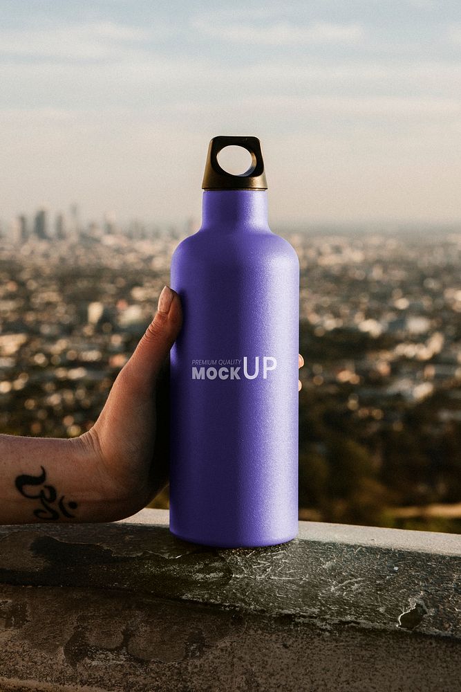 Hand holding a purple stainless steel bottle mockup with urban view