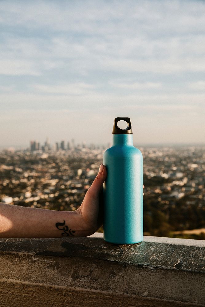 Hand holding a turquoise stainless steel bottle with urban view
