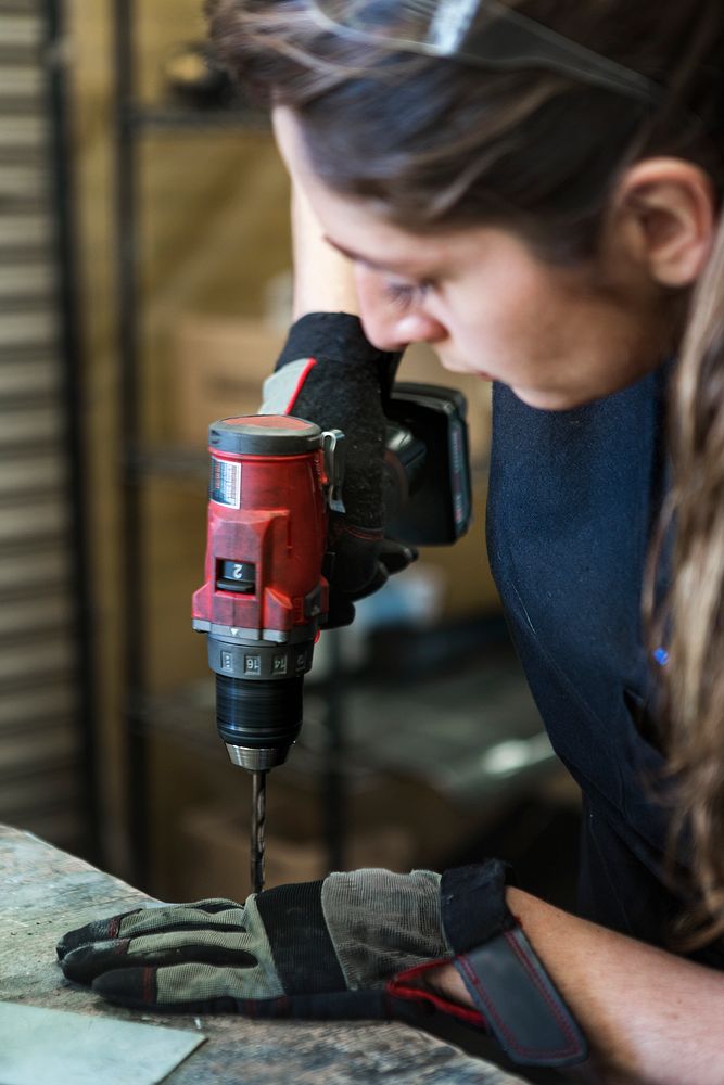 Female mechanic drilling into metal