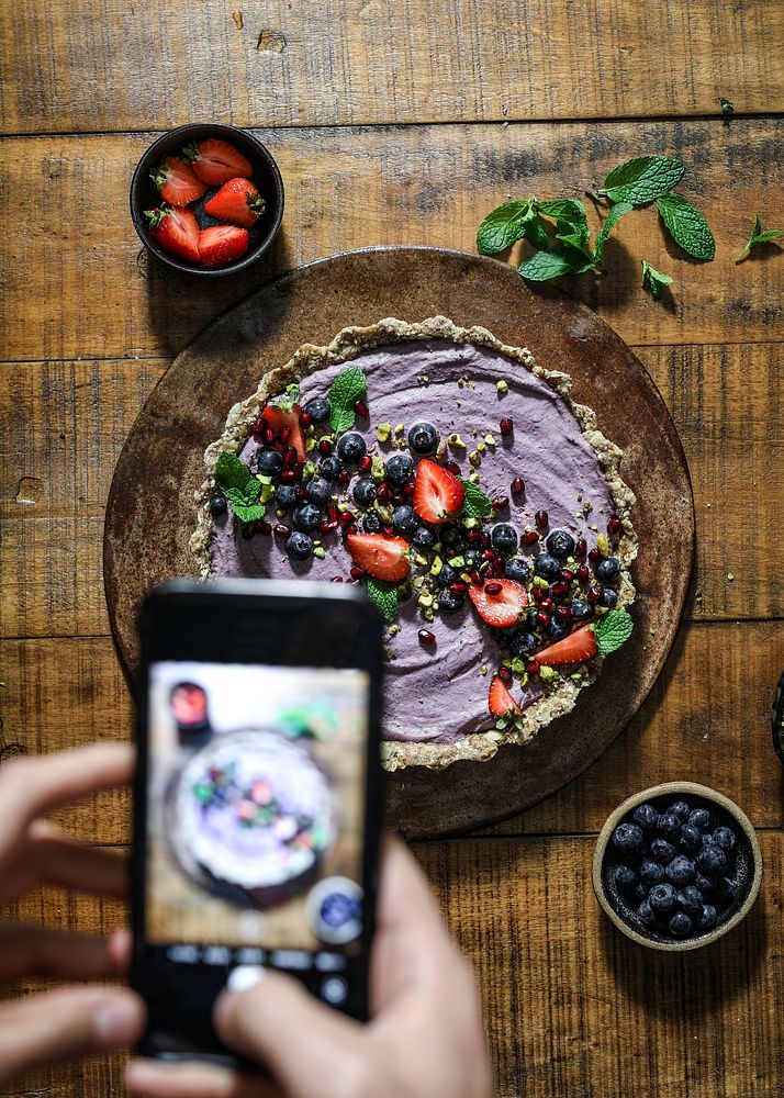 Woman taking a photo of sweet potato tart topped with strawberries and blueberries