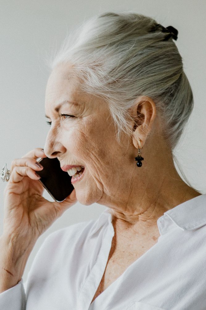 Cheerful senior woman talking on a phone in a white room