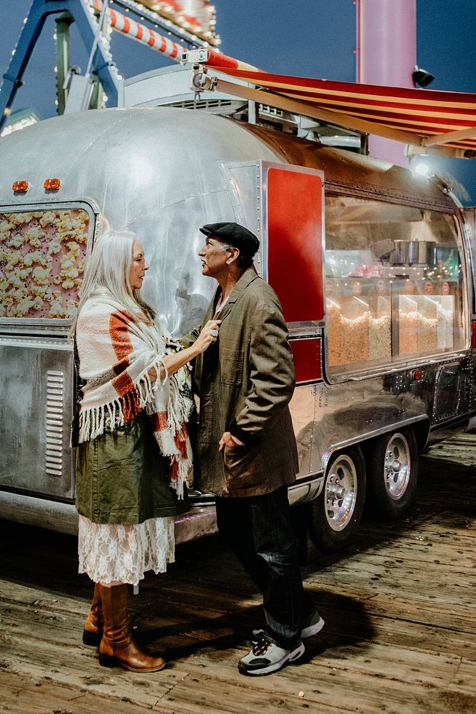 Cool senior couple standing by the food truck inside of an amusement park