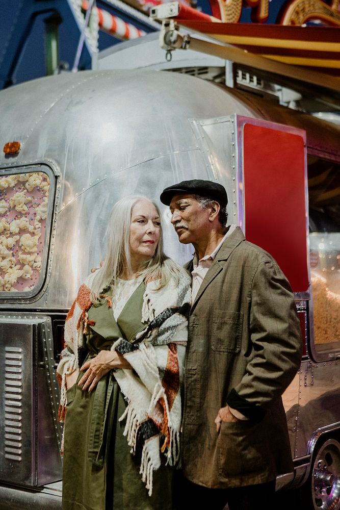 Cool senior couple standing by the food truck inside of an amusement park