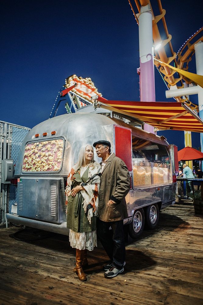 Cool senior couple standing by the food truck inside of an amusement park