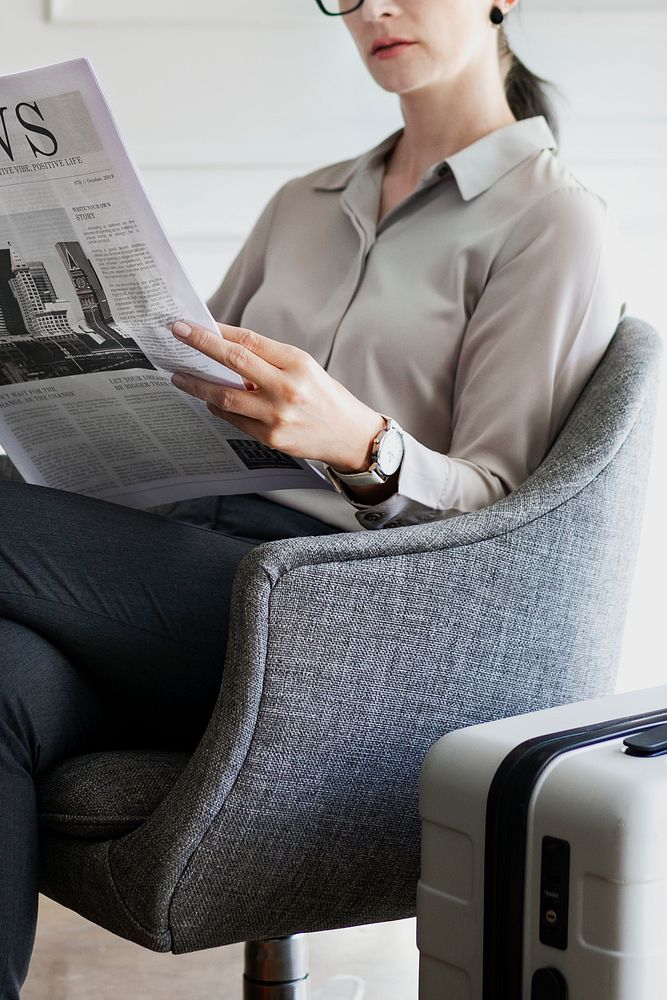 Businesswoman with a suitcase reading a newspaper