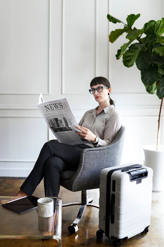 Businesswoman with a suitcase reading a newspaper