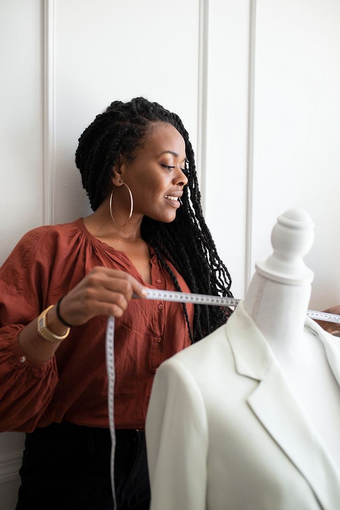 Black fashion designer measuring a white coat on a pinnable mannequin