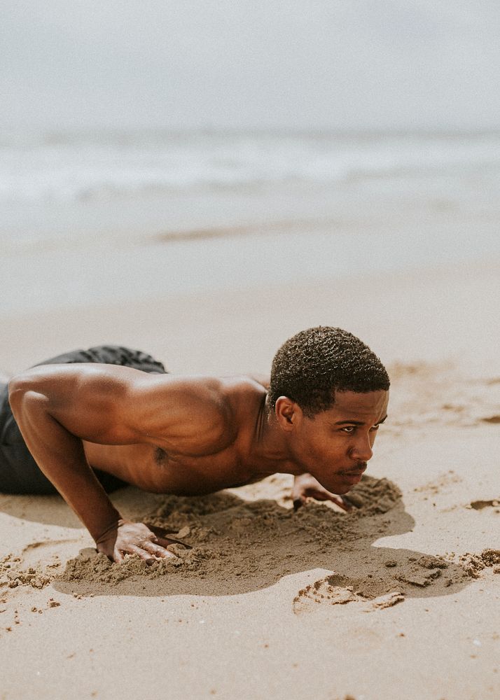 Muscular black man doing pushups at the beach