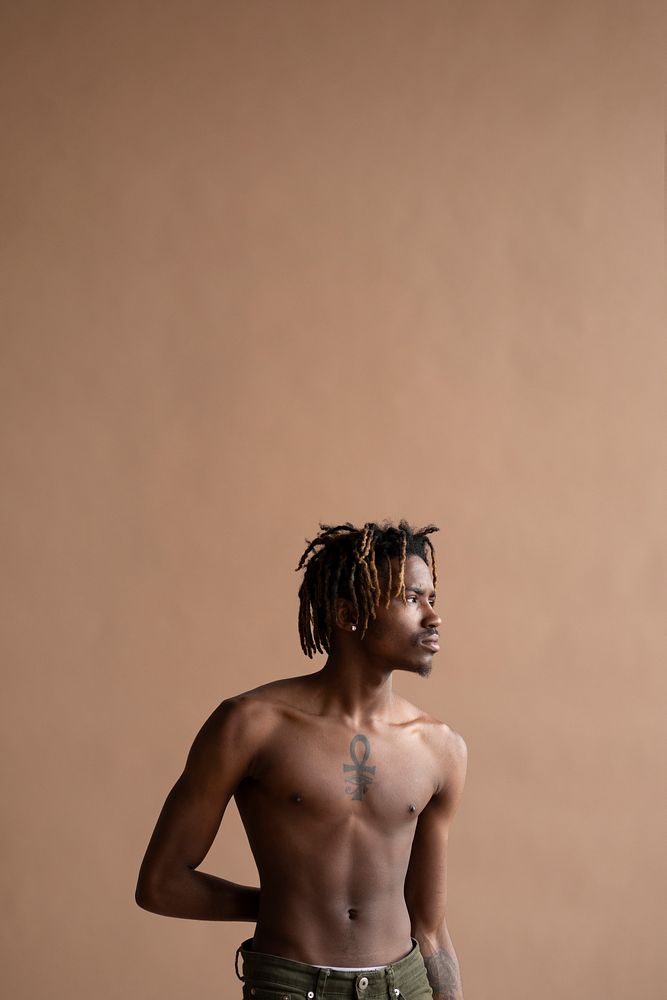 Black shirtless man posing by a beige wall