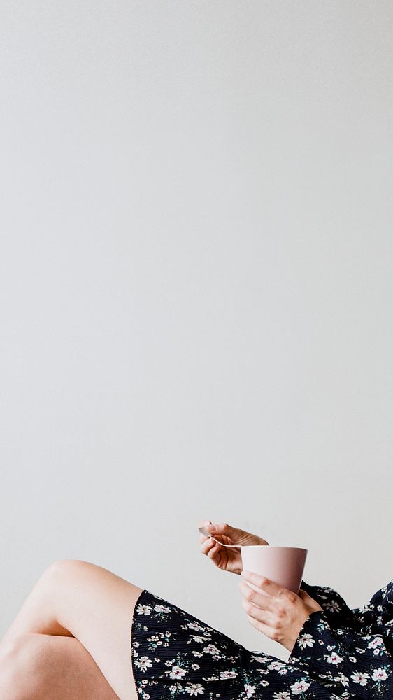 Woman sitting by a white wall with a cup of tea