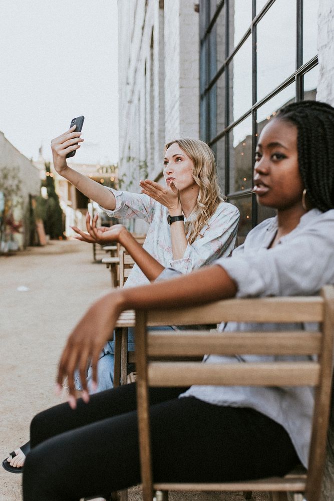 Black woman getting bored of her blond friend keep taking a selfie