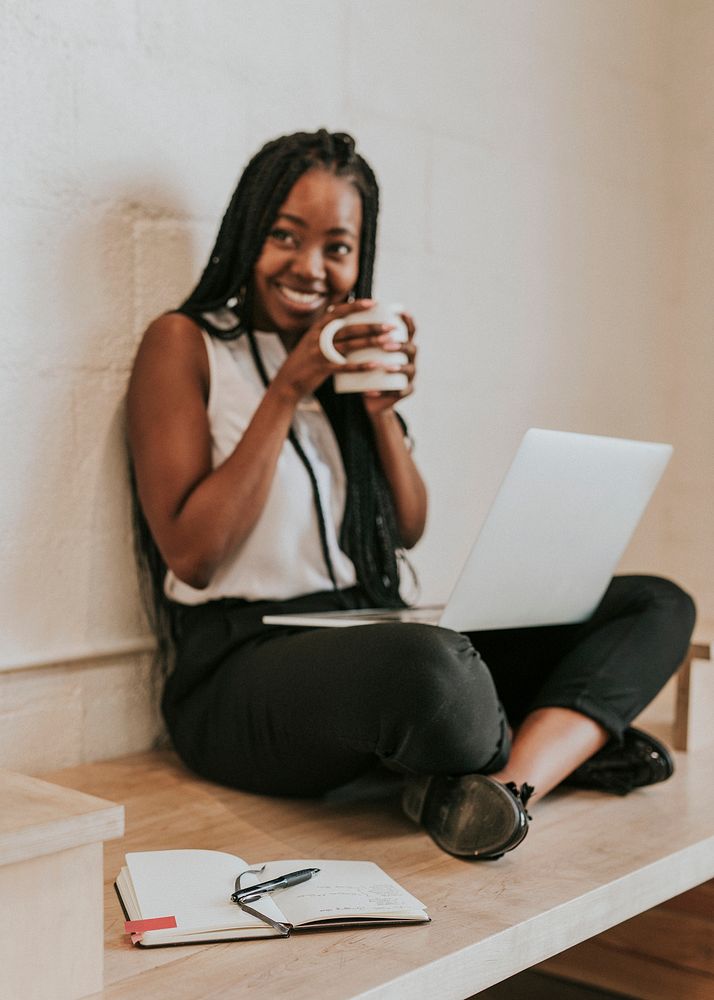 Black woman using a notebook on her laps on a wooden floor