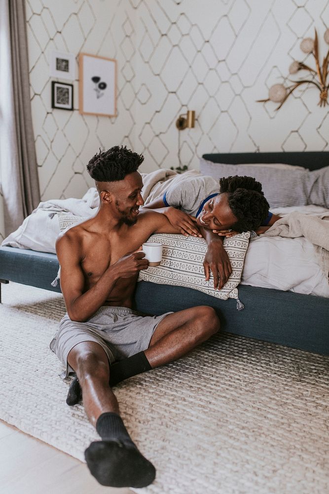 Happy black couple enjoying a conversation in bed while drinking coffee