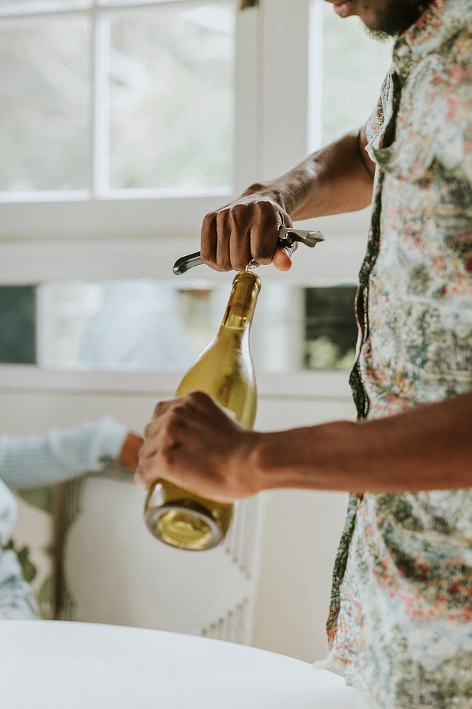 Black man uncorking a white wine bottle