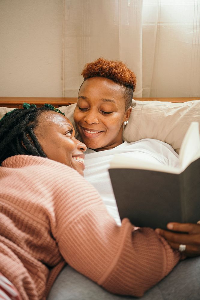 Happy lesbian couple cuddling and reading a book together