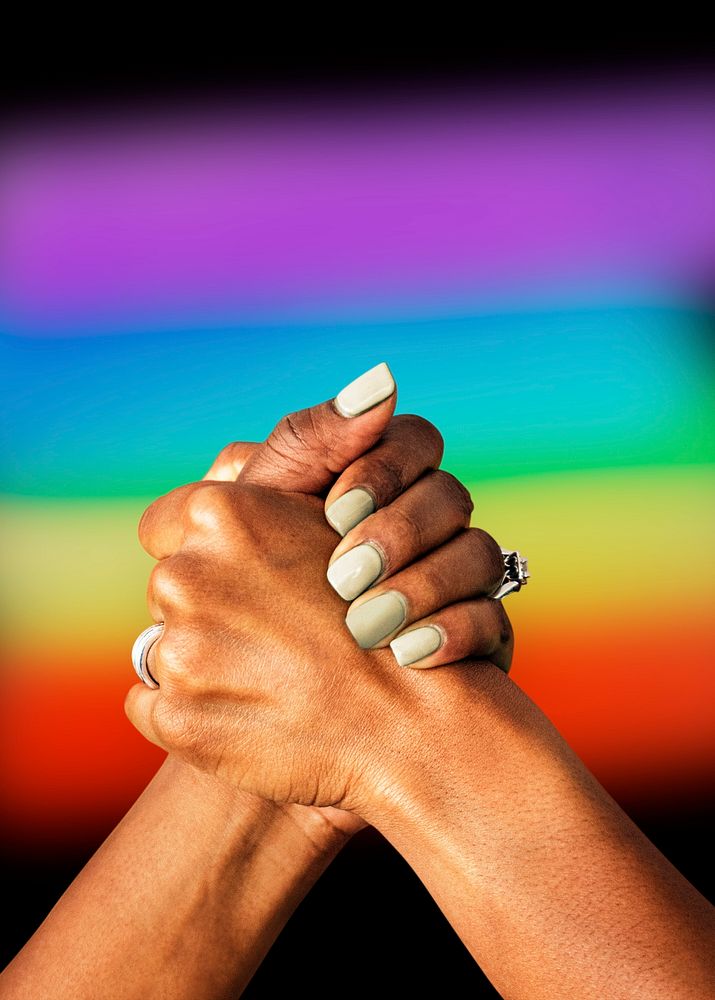 Gay couple holding hands in front of a rainbow flag signifying support and love
