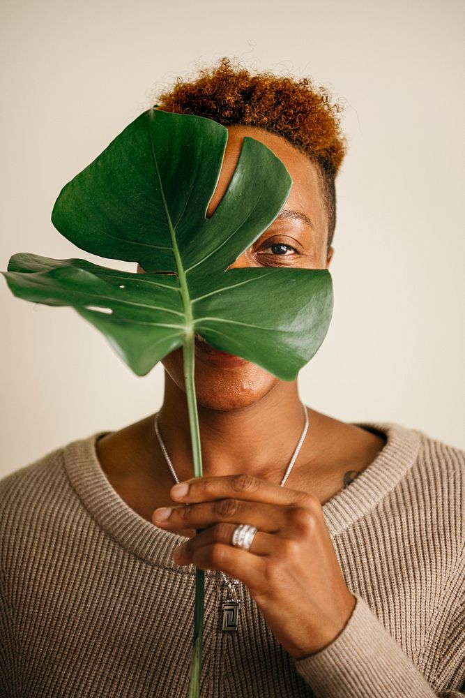 Happy black woman holding a leaf over her face