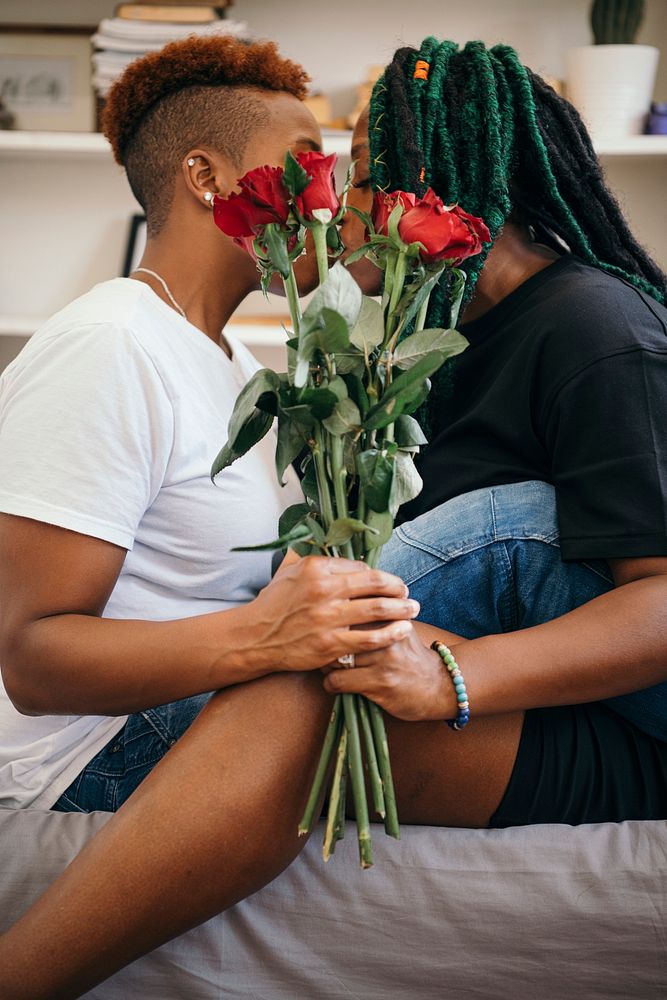 Happy lesbian couple holding roses and kissing in the bedroom