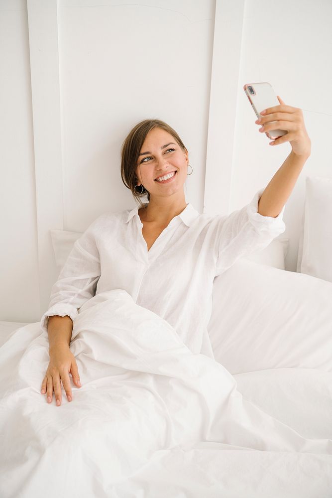 Cheerful woman taking a selfie on a white bed