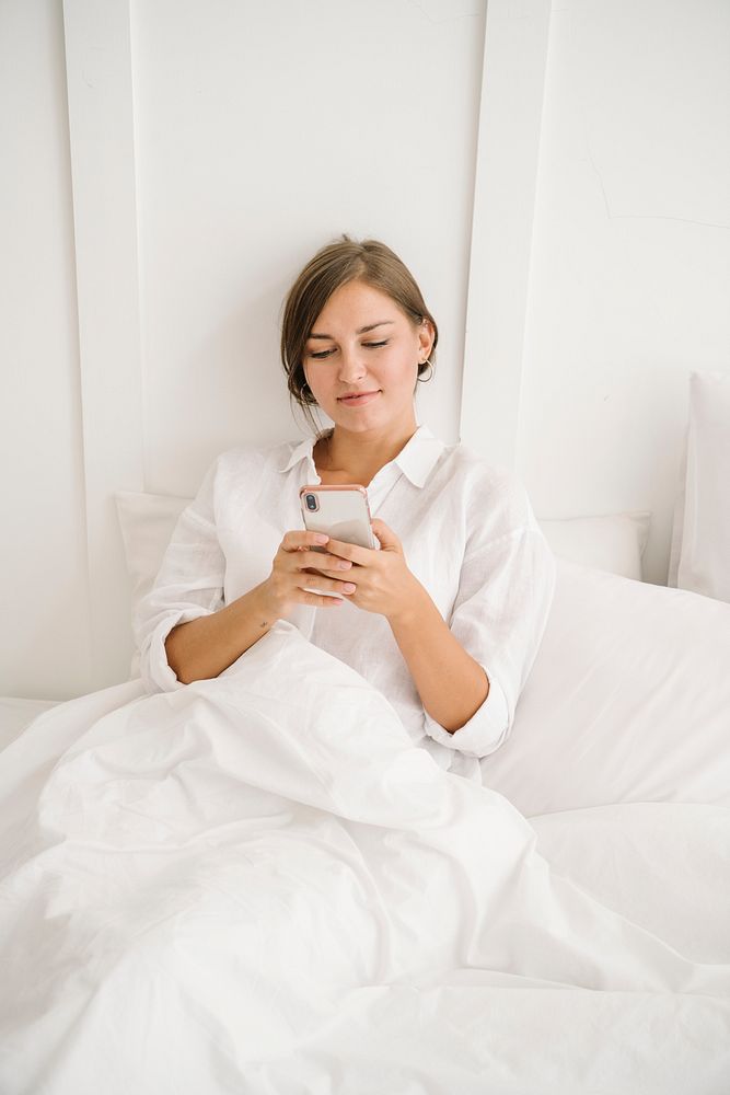 Woman using a phone on her white bed
